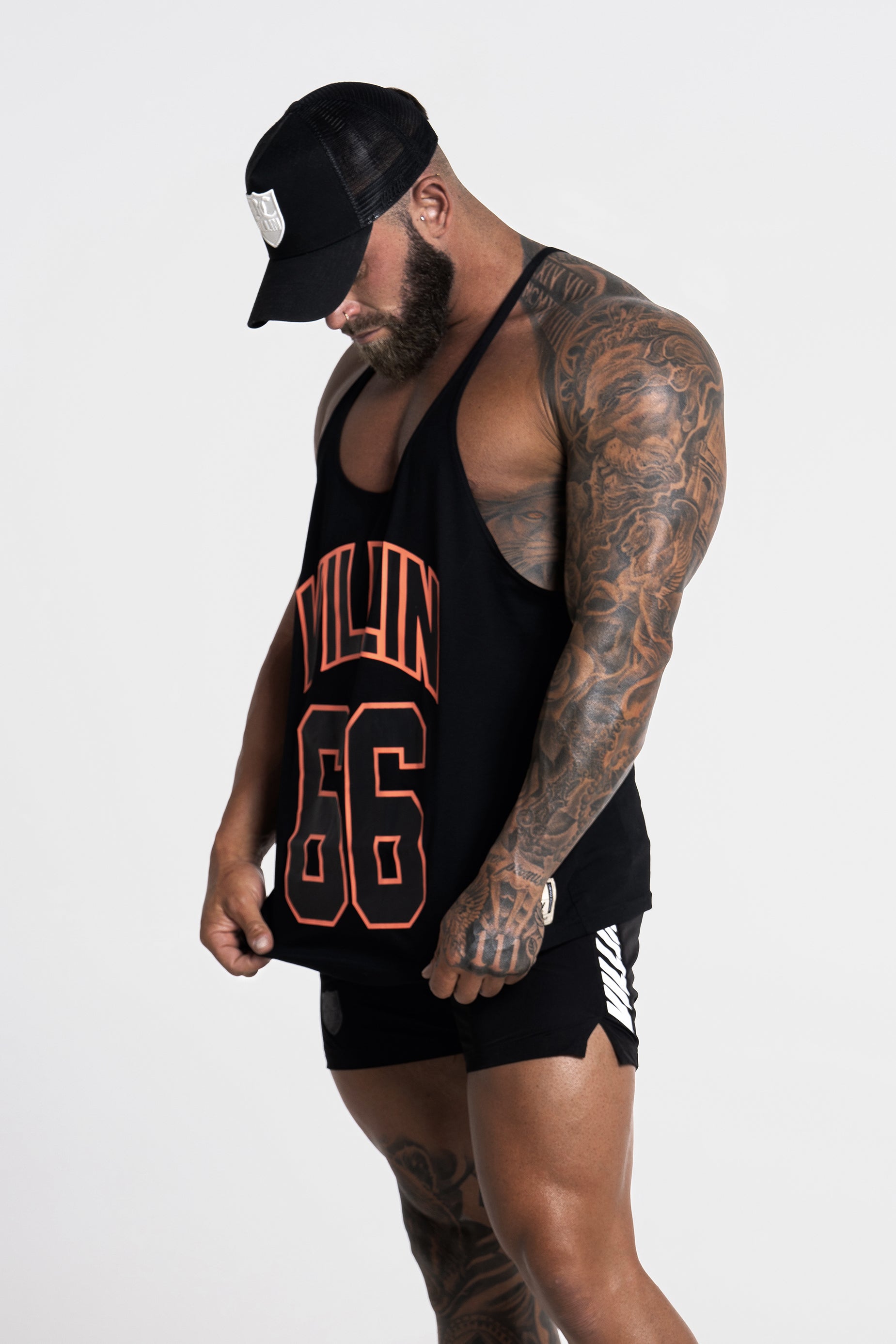 Man wearing a black VILLIN tank top with orange text and black shorts on a white background